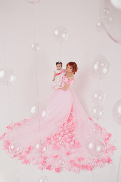 The child in the arms of his mother in a pink dress of flowers