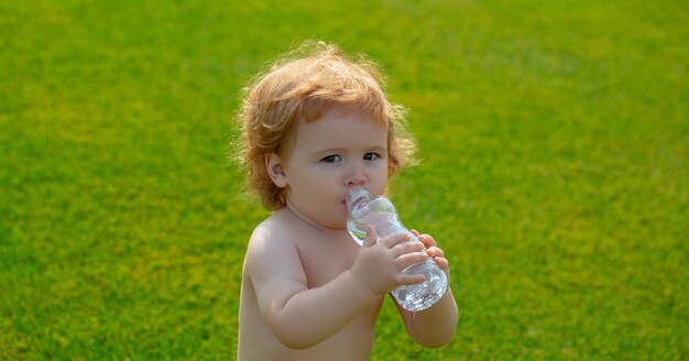 Child baby resting in grass park on nature drinks clean water in summer grass park