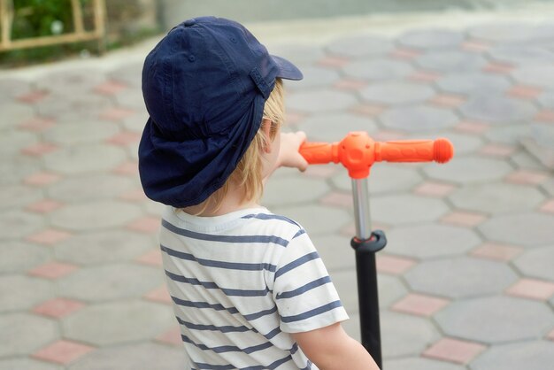 A child in a baseball cap holds the wheel of a scooter