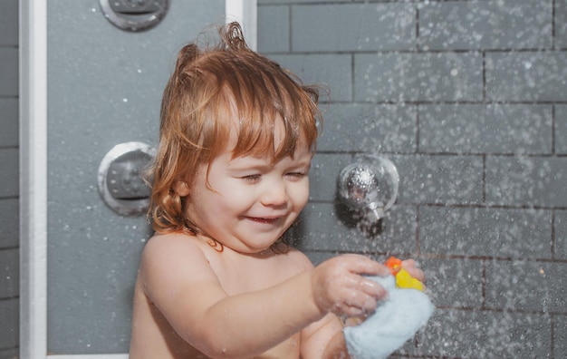 Child bathes in a shower bathing baby happy kid with soap foam on head