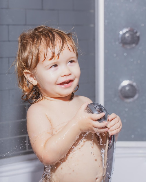 Child bathing under a shower funny baby kid bathed in foam and washing in bathtub at home