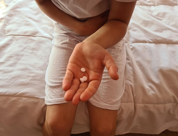 Ребенок в постели с болью в животе держит медицинские таблетки