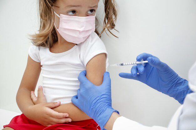 Child being vaccinated against covid 19 goes back to medical school with blue glove and syringe