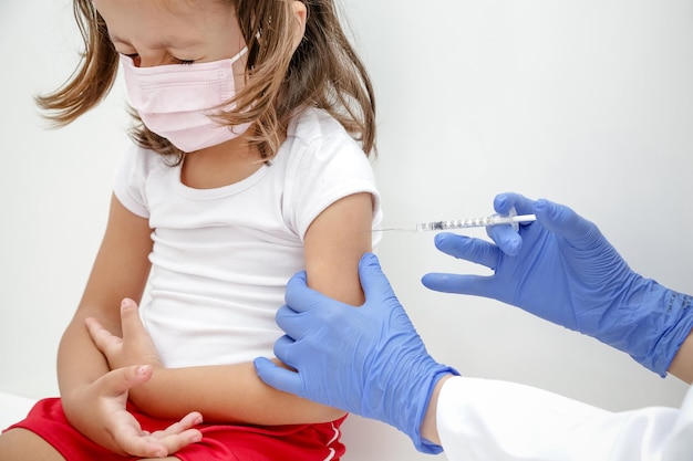 Child being vaccinated against covid 19 goes back to medical school with blue glove and syringe