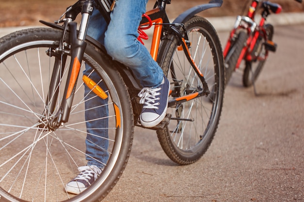 晴れた春の日にアスファルトの道路で自転車に乗る子。ペダルと足のクローズアップ