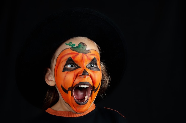 Un bambino con un cappello nero e un trucco di zucca urla, isolato.