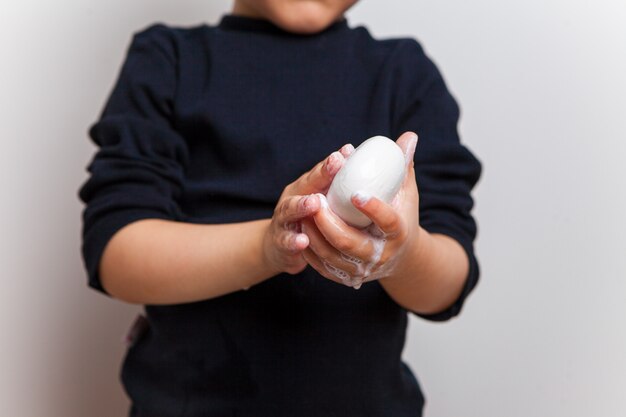 Child, in a black T-shirt, hands in soapy solution hold soap on a white studio background. Hand disinfection. Soaped palms and fingers. Isolated