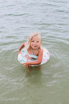 La ragazza bionda del bambino con un anello di gomma è giocata nel mare.