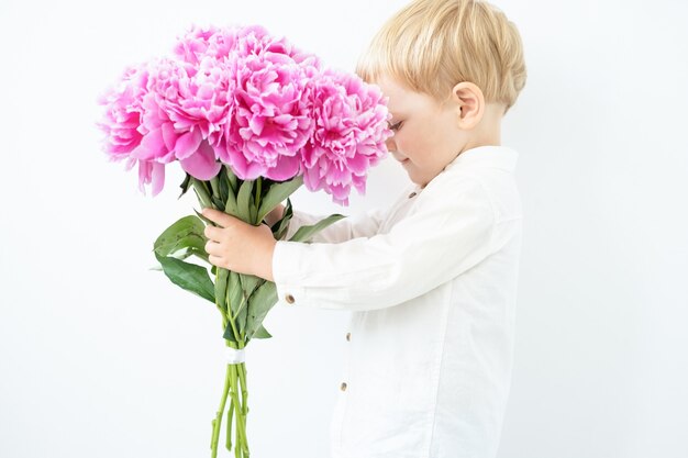 Child blonde boy with big bouquet of pink peonies on white background love and romantic concept