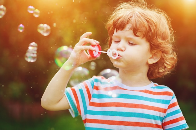 Child blowing soap bubbles in summer park.