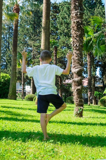 Child boy of 7 years old pulls hands to sun doing yoga and
looks up at palm trees back view dreaming and meditation zen like
concept relaxation travel vacation kids