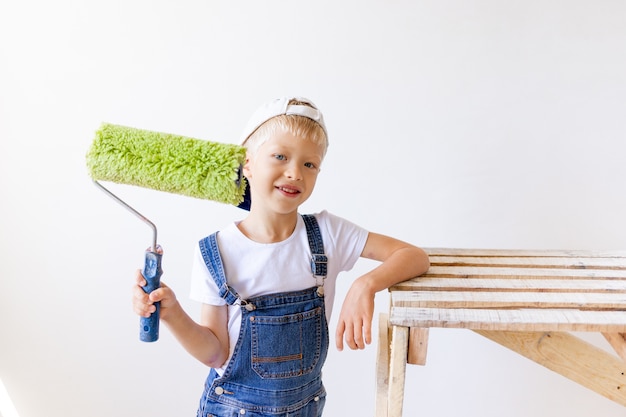 Il bambino ragazzo builder fa riparazioni in un appartamento, un operaio vuole dipingere le pareti con un rullo