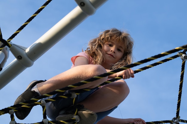 Child boy climbed on top of the rope web on playground little\
boy climbs up the ladder on the playground child climbs up the\
ladder kid boy climbing the net