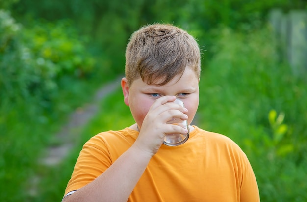 子供の男の子はグラスから水を飲みます。