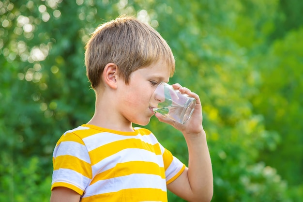 子供の男の子はグラスから水を飲みます。