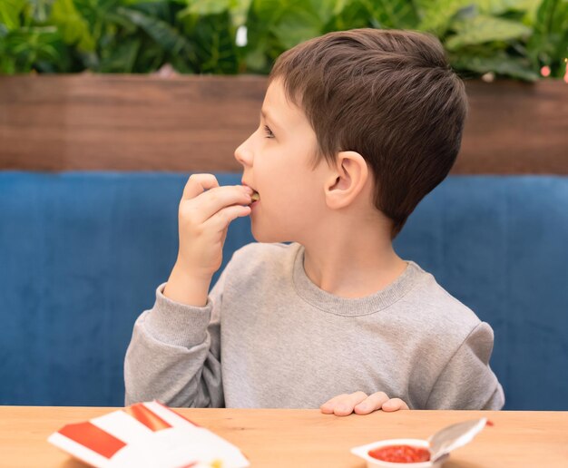 Child boy eating his French fries with ketchup in the cafe Junk food unhealthy eating concept