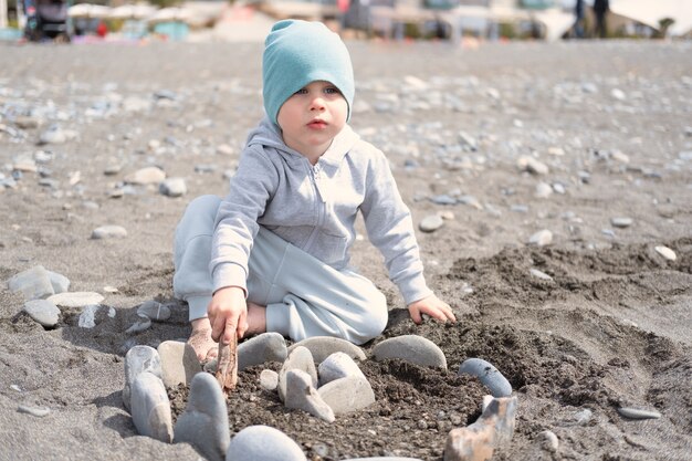 Child boy folds castle of stones play with rocks on the shore on a sunny day