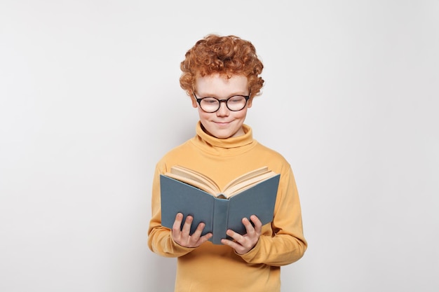 Child boy in glasses reading a book on white background