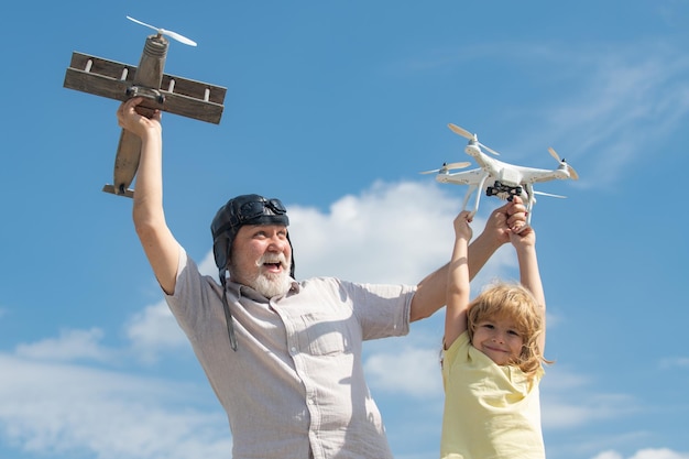하늘을 배경으로 장난감 비행기와 쿼드콥터 드론을 가지고 노는 소년과 할아버지 어린이 조종사 비행사