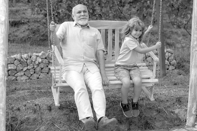 Foto bambino ragazzo e nonno oscillante nel giardino estivo nonno e nipote seduti sull'altalena nel parco