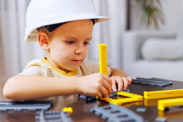 Photo child boy in helmet playing and building with colorful plastic bricks at table