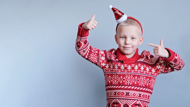 写真 子供、クリスマスの赤い帽子と灰色の背景のセーターの男の子。新年とクリスマスのコンセプト。