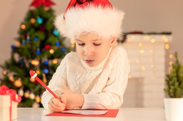 산타 클로스 크리스마스 또는 새해 아늑한 휴일 개념 크리스마스 시간 선택적 초점에 편지를 쓰는 빨간 산타 모자에 아이 소년