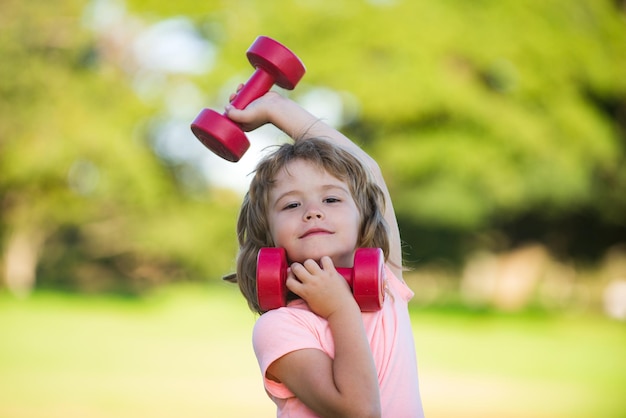 Child boy is doing exercises with dumbbells in summer park healthy activities kids lifestyle