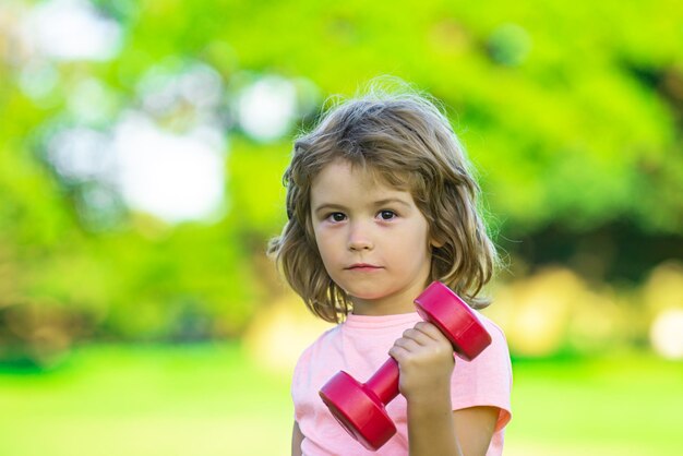 Child boy is doing exercises with dumbbells in summer park sport portrait kids