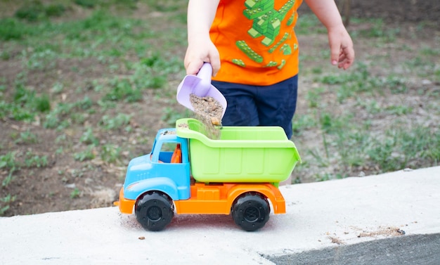 子供の男の子がおもちゃの車とおもちゃのトラックの子供の屋外ゲームでサンドボックスで遊んでいます