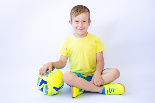 Ребенок мальчик сидит на белом фоне с футбольным мячом в руках спорт