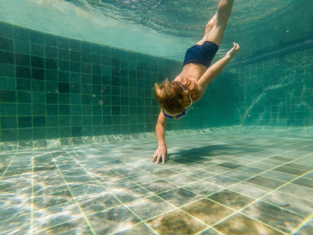 Photo a child boy is swimming underwater in a pool, smiling and holding breath, with swimming glasses