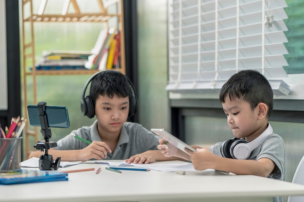 Il ragazzo del bambino sta usando comunica su internet a casa. homeschooling, apprendimento a distanza, ragazzino asiatico che tiene una lezione online e felice per la quarantena di homeschool.