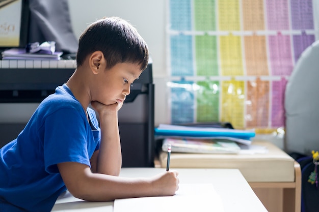 子供男の子は部屋で本を書いています。