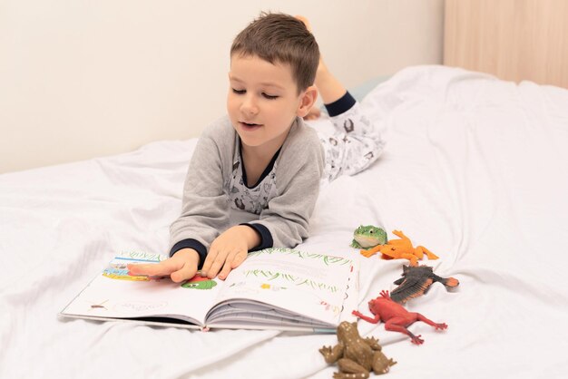 Child boy lies on the bed and reads a book to his toys Relaxing at home concept