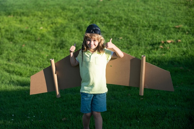 緑の草に対しておもちゃの翼を持つパイロットのような子供の少年は、子供の自由の概念になることを夢見ています