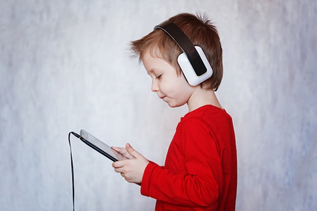 Child Boy listening to music or watching movie with headphones and using digital tablet.