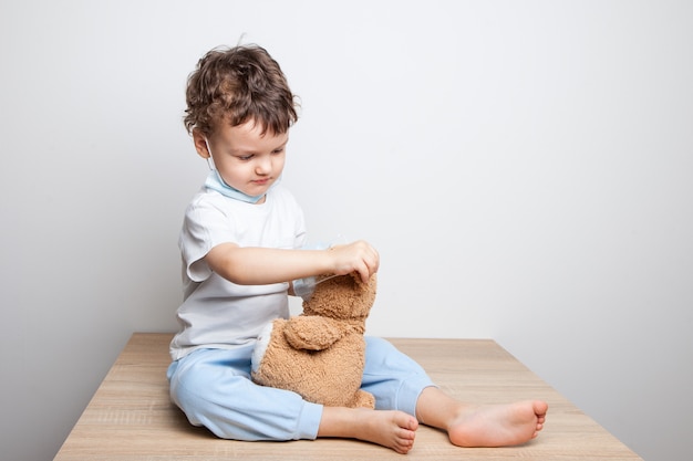 Child, a boy in a medical mask puts on a mask on a teddy bear. Teaching a child to protect and prevent quarantine from cornavirus