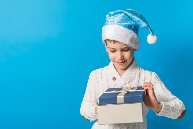 Child boy open gift kid in blue christmas hat holds gift box shopping time copy space and empty