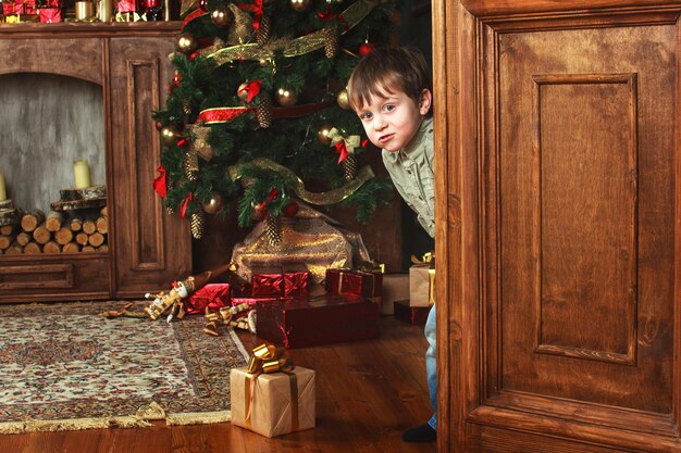 Child boy peeks out of the door with a christmas gift box.