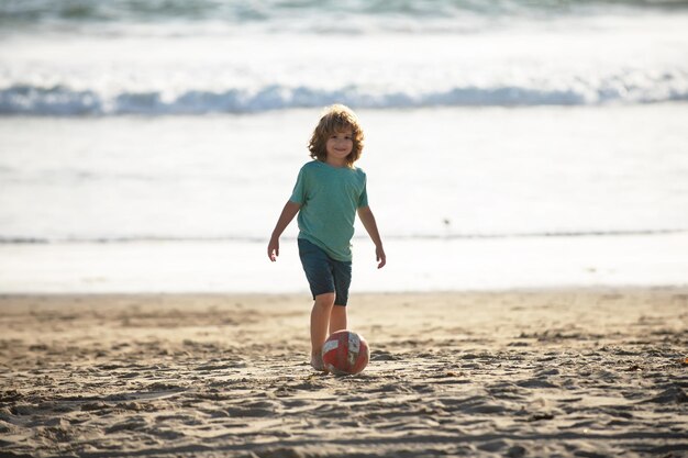 Child boy play football on sand beach