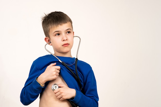 Ragazzo del bambino che gioca al dottore con lo stetoscopio in mani. concetto di pediatria, assistenza sanitaria e persone.