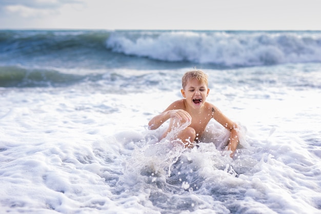 Child boy playing in the waves on the beach in summer sunset
