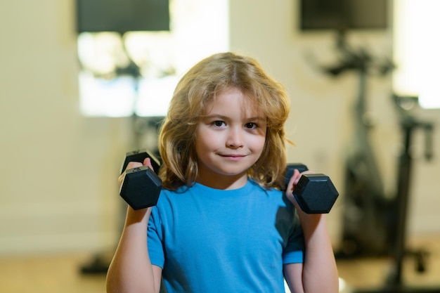 Child boy pumping up biceps muscles with dumbbell Child workout kid in gym Fitness kids with dumbbells