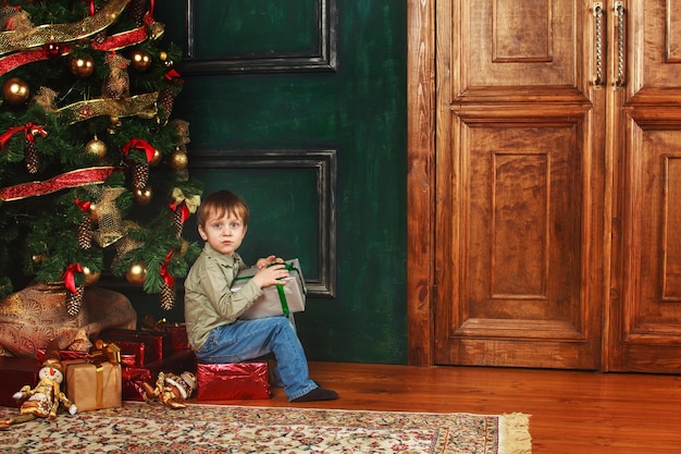 Child boy sitting under the Christmas tree with gift box