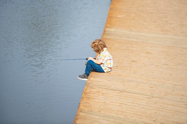 Child boy sitting near the lake and fishing kids hobby smiling child fishing on the lake boy with sp