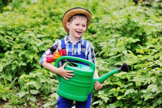 Child boy in a straw hat in a blue work suit gardener with a bouquet of tulips and a green watering can