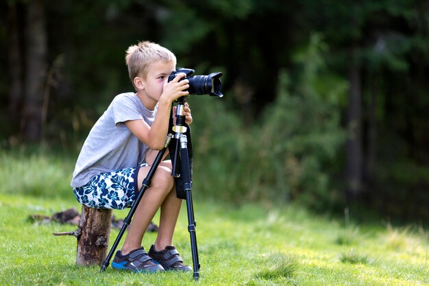 Child boy taking picture with tripod camera.