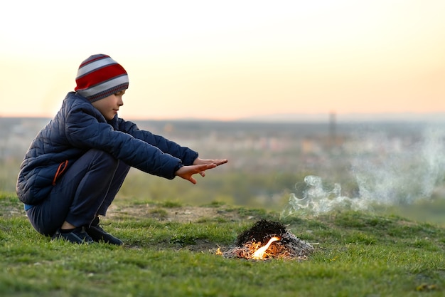 Child boy warming near bonfire outdoors in cold weather.