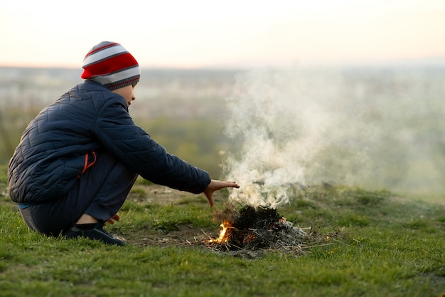 Child boy warming near bonfire outdoors in cold weather